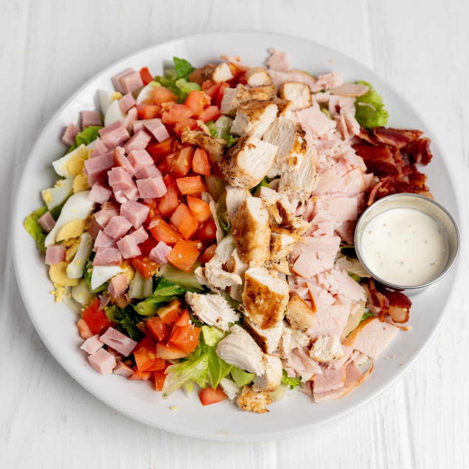 Loaded chef salad with lettuce, grilled chicken, ham, turkey, bacon, tomatoes, eggs, and creamy dressing.