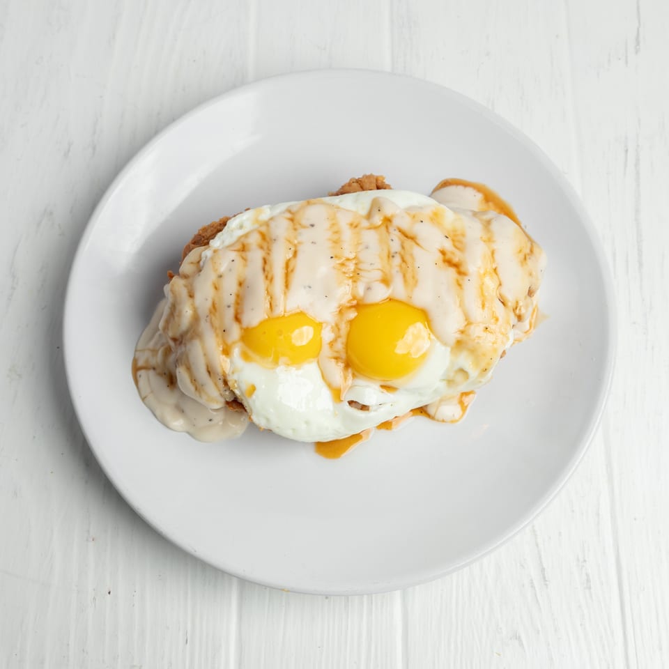 Biscuit topped with creamy pepper gravy and two sunny-side-up eggs on a white plate.