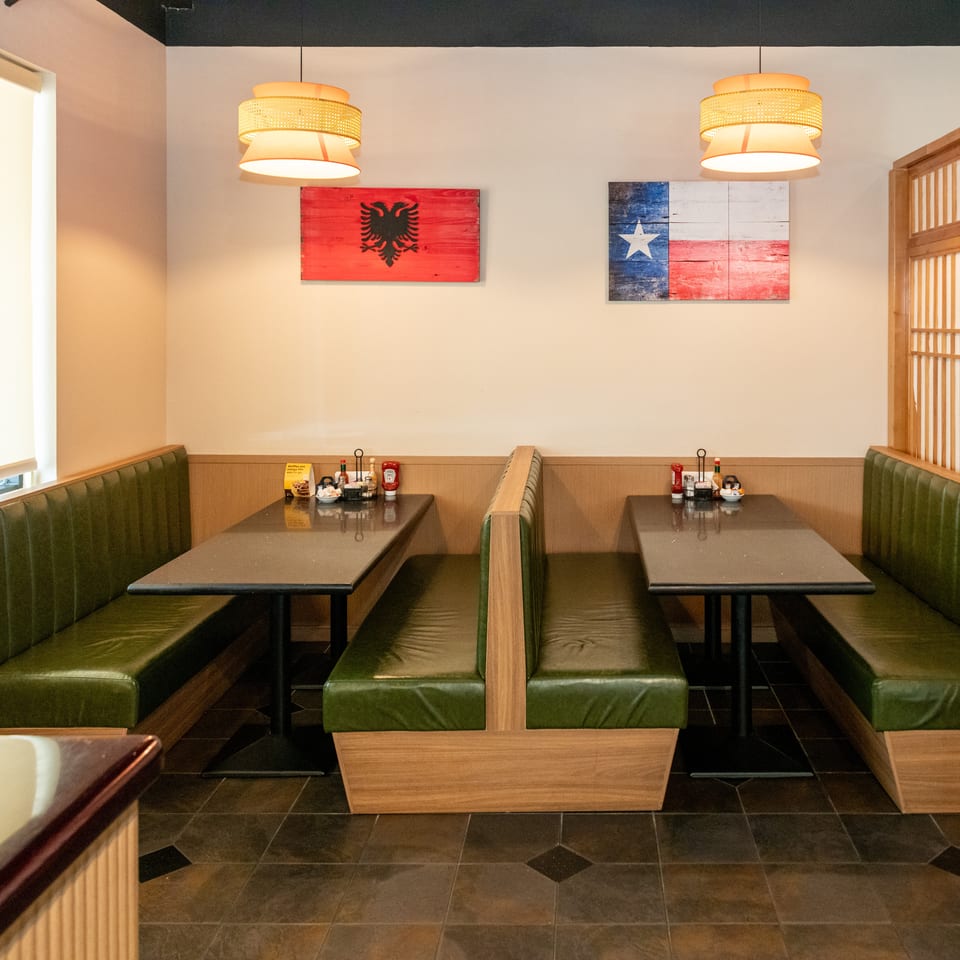 Restaurant dining area with green leather booths, pendant lights, condiments, and Albanian and Liberian flag artwork.