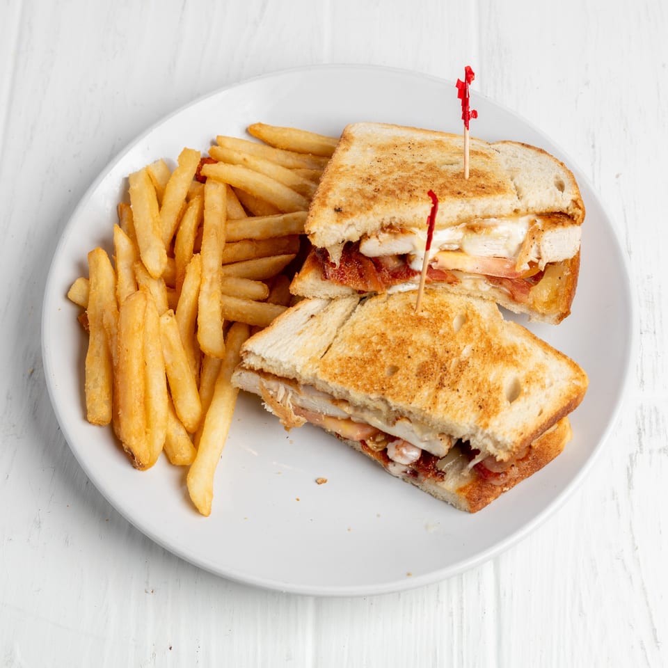 Toasted chicken, bacon, and cheese sandwich halves with French fries on a white plate.