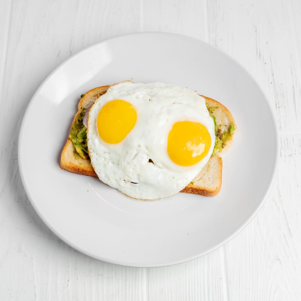 Avocado toast topped with two sunny-side-up eggs on a white plate.