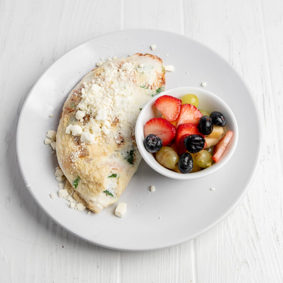 Cheese-topped stuffed breakfast pastry served with a bowl of strawberries, blueberries, grapes, and sliced fruit.
