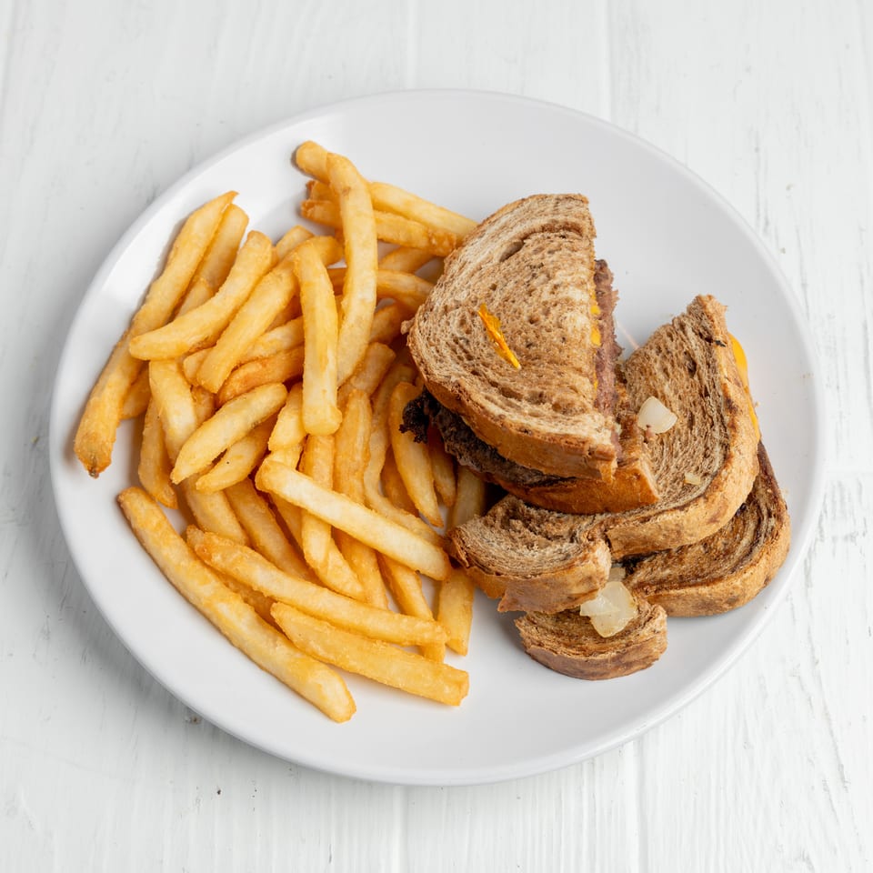Grilled sandwich with melted cheese and onions served alongside golden French fries on a white plate.