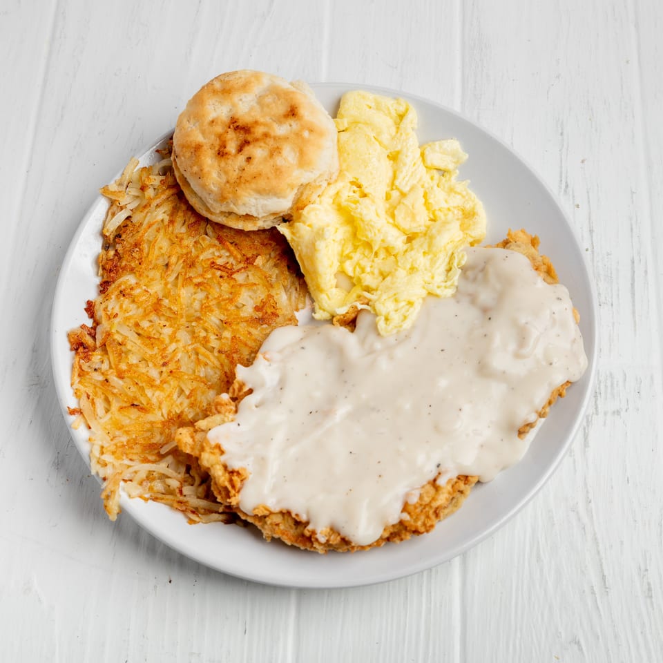 Southern breakfast plate with fried chicken smothered in gravy, scrambled eggs, hash browns, and a biscuit.