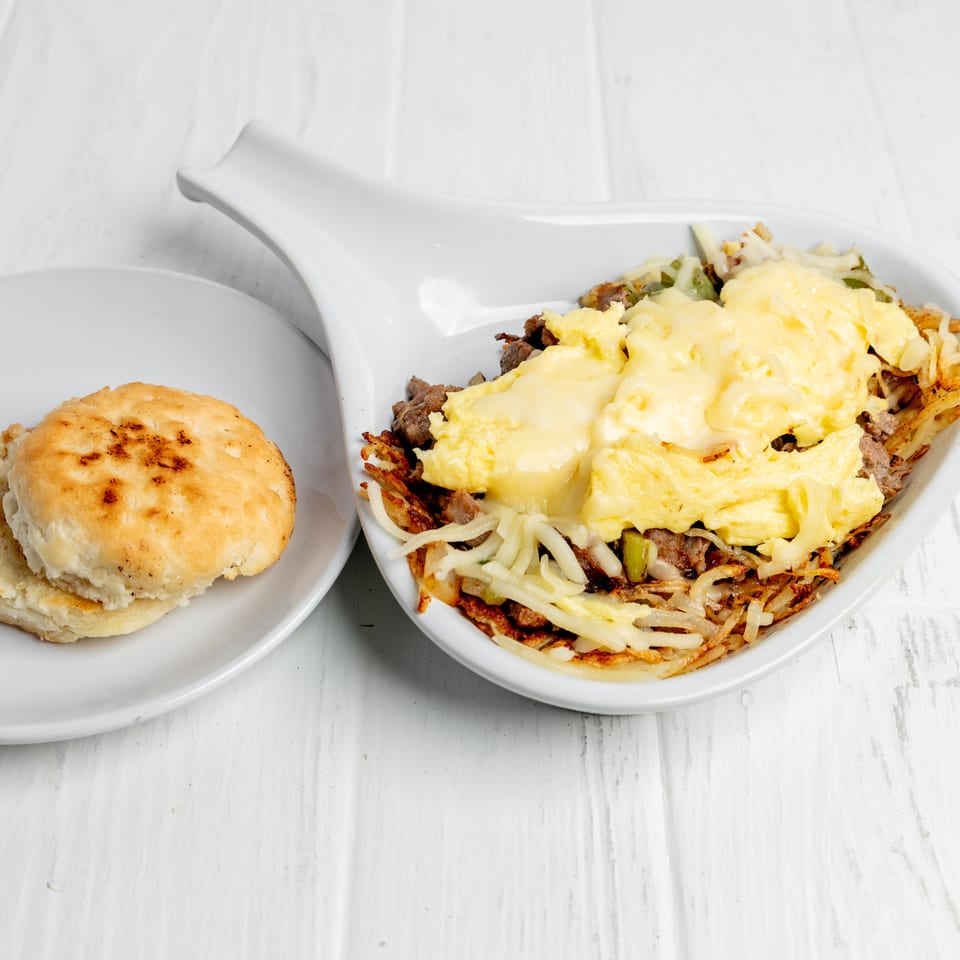 Cheesy scrambled eggs with sausage and hash browns served alongside a toasted biscuit on white plates.