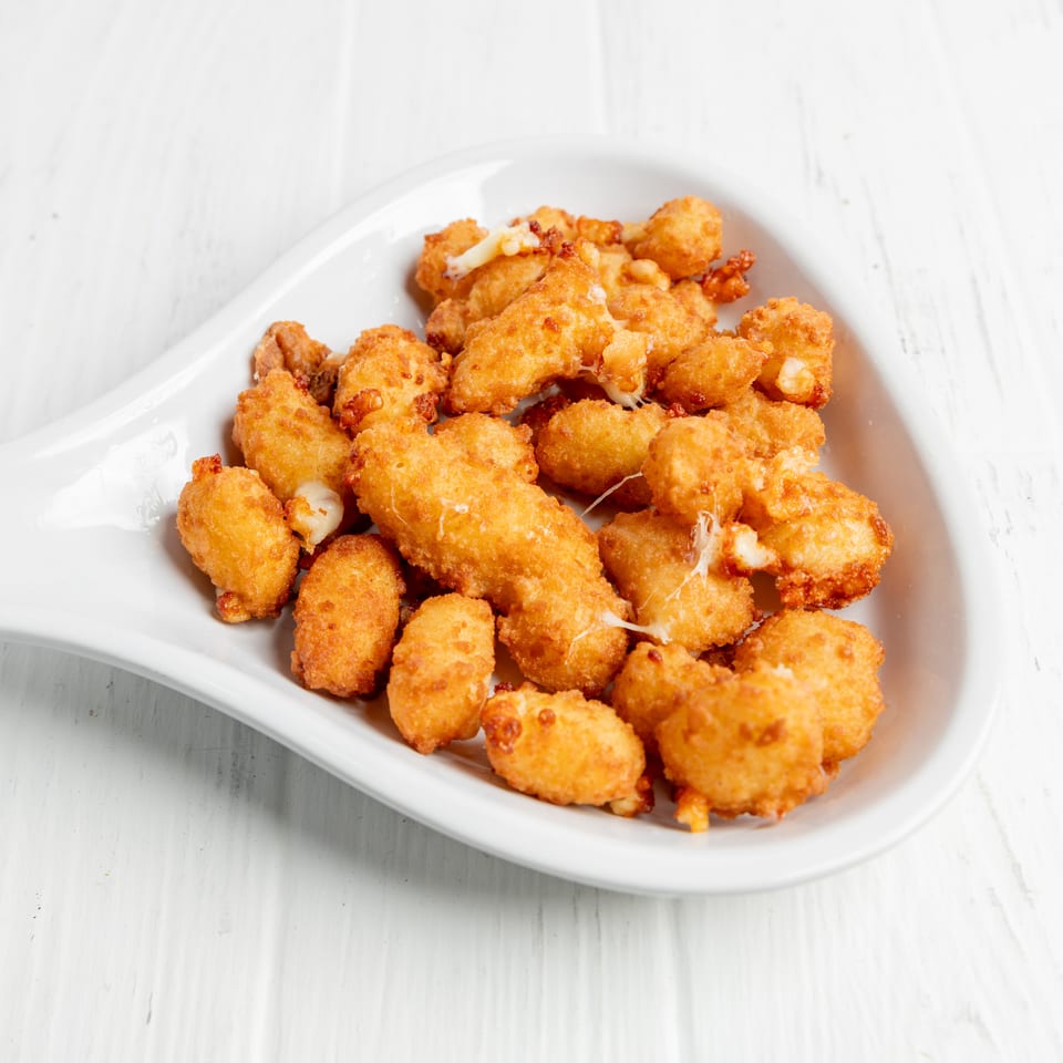 Golden-brown breaded cheese curds piled on a white serving platter atop a white wooden table.