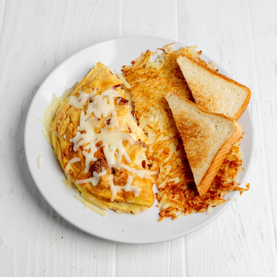 Plate of cheese-topped omelet with crispy hash browns and toasted bread on a white wooden table.