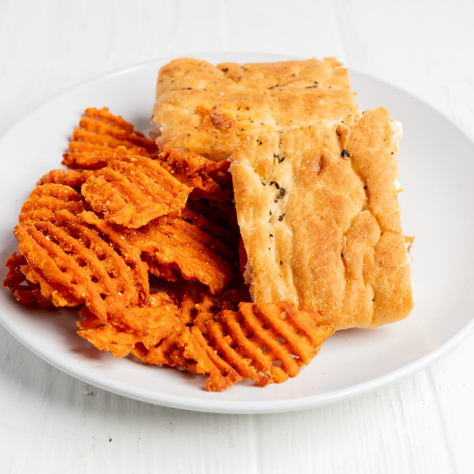 Plate of golden fried waffle-cut potatoes and seasoned rectangular pastries on a white table.