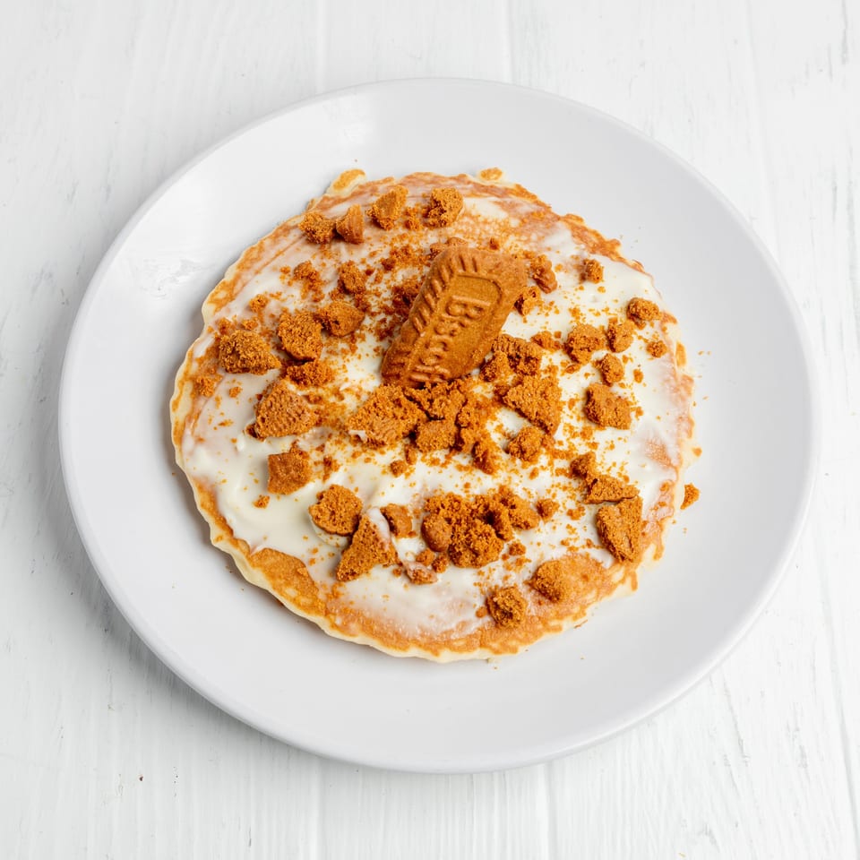Pancake topped with white icing, crushed cookies, and a whole sandwich cookie on a white plate.