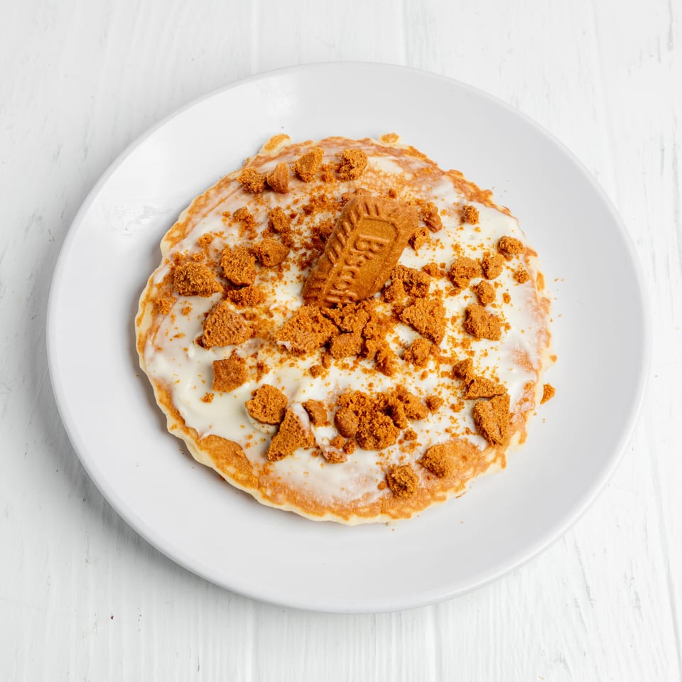 Pancake covered with white icing, cookie crumbs, and a whole cookie on a white plate.